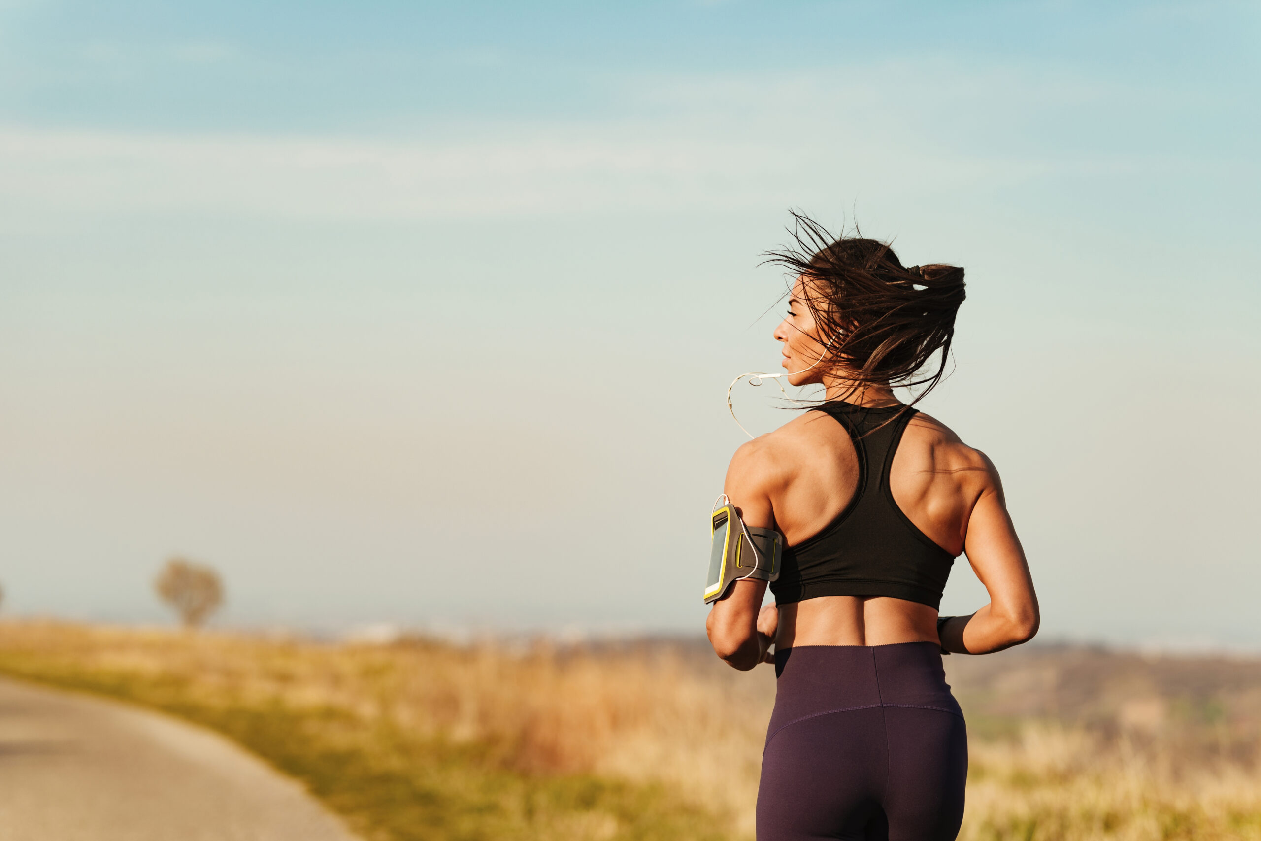 Rear view of muscular build woman running in nature.